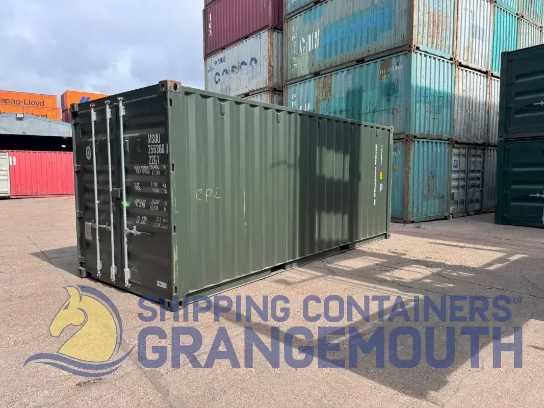 A green shipping container is situated among stacks of other containers in a storage yard.