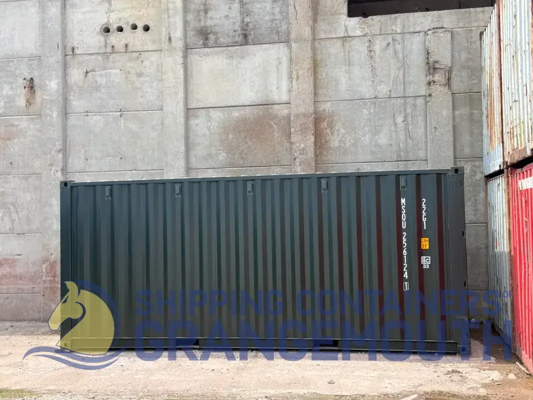 A green shipping container beside a concrete wall, with colorful containers stacked on the right.