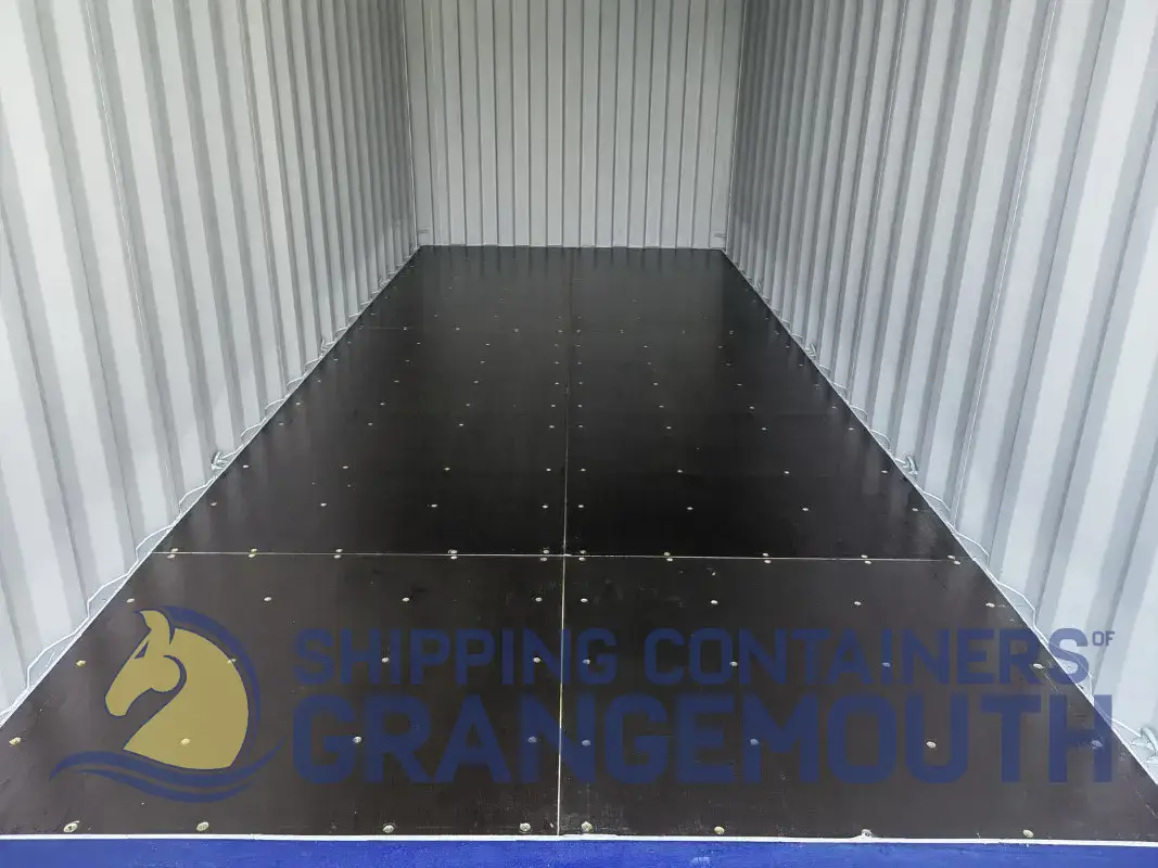 An empty shipping container interior with a dark floor and light metallic walls, featuring a logo at the bottom.