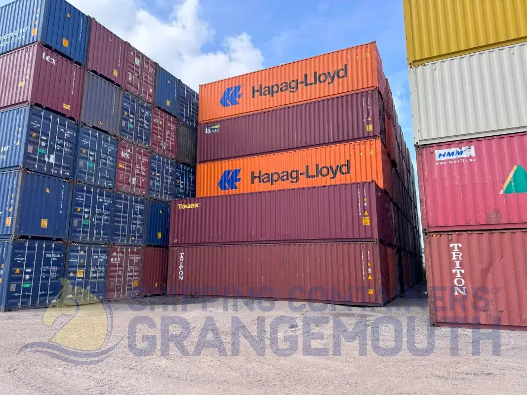 Stacked shipping containers in various colors, featuring brands like Hapag-Lloyd and Triton, under a blue sky.