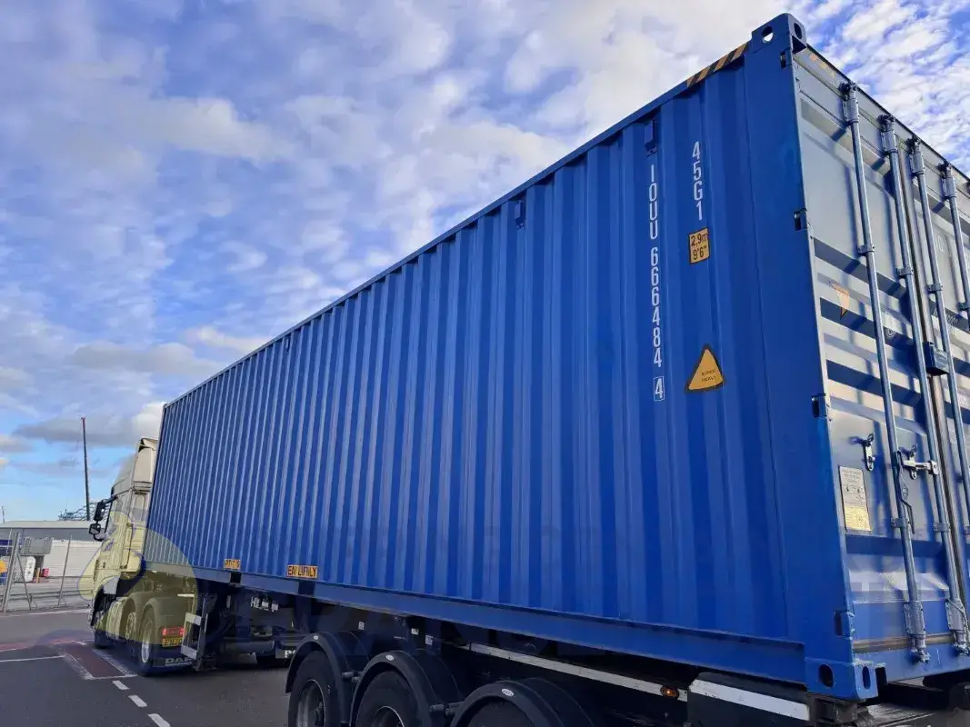 A blue shipping container mounted on a truck, with a cloudy sky in the background.