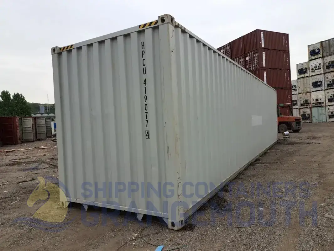 A large, empty shipping container in a storage area with other containers in the background.