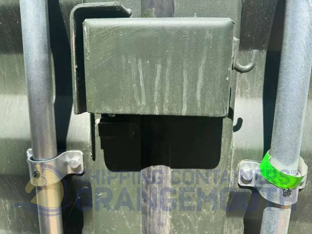 A close-up of a green container latch with metal bars and markings. Detailed and industrial appearance.